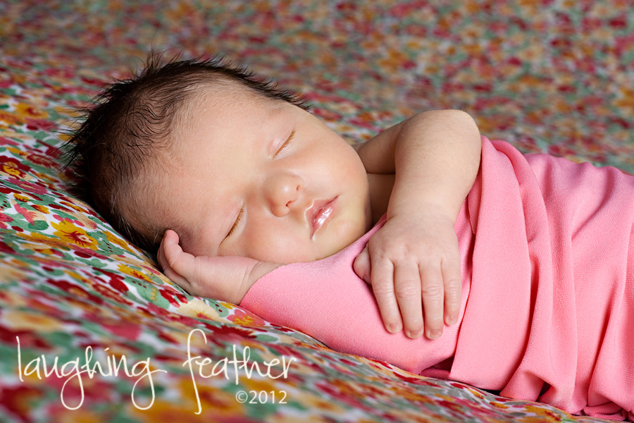 Newborn in pink wrap on floral backdrop